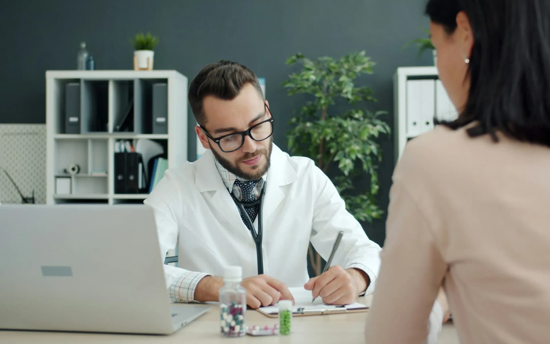 A doctor in a white coat taking notes during a consultation